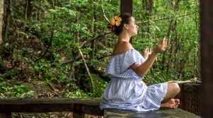Beautiful young girl in a dress is meditating in the rain forest on the stone